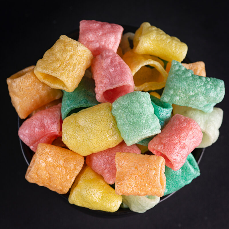 A bowl of fruit flavored snacks on top of black background.