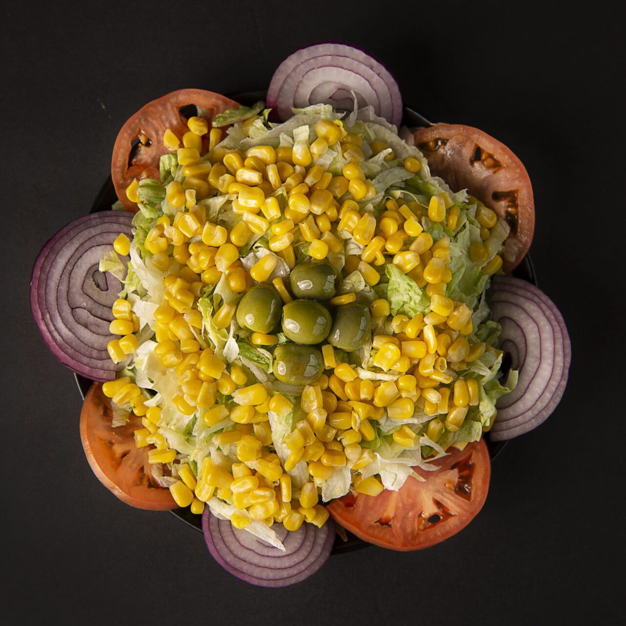 A bowl of corn, tomatoes and onions on top of black surface.