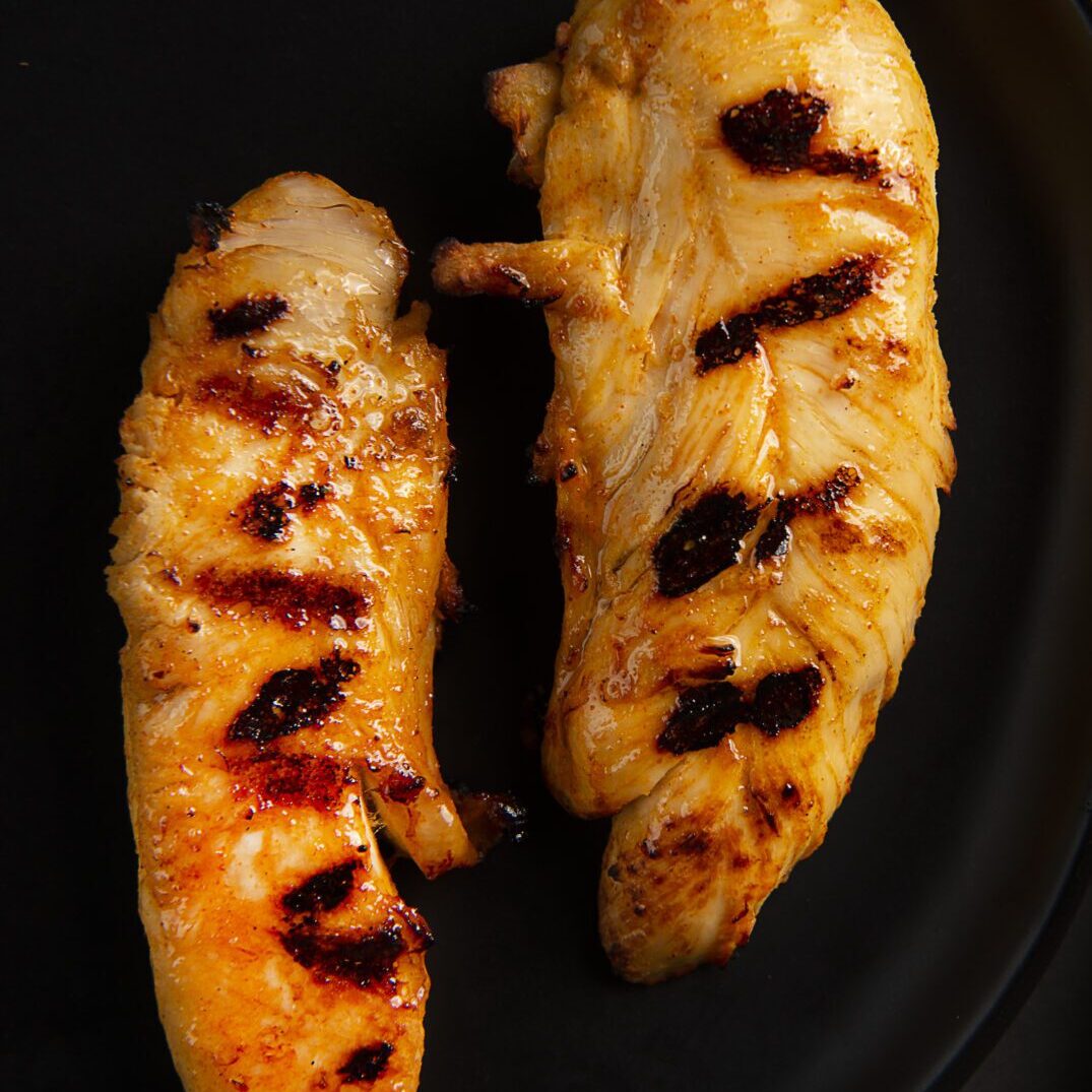 Two pieces of grilled chicken on a black plate.