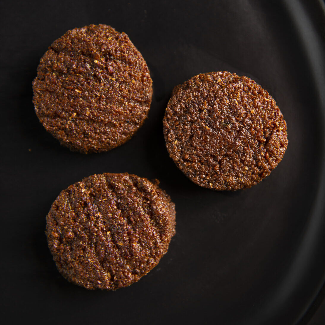 Three hamburger patties are sitting on a black plate.