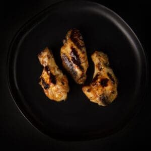 Three chicken wings on a black plate.